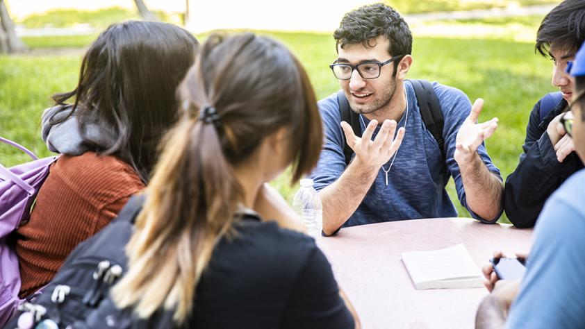 Group of five students talking at a table outside