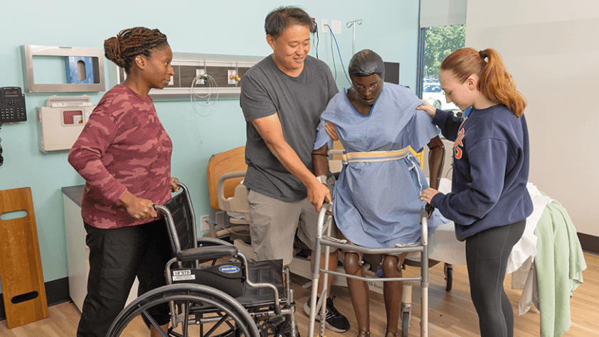 Three students practicing occupational therapy techniques with a mannequin