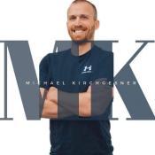 Male in navy blue shirt smiling with his arms folded acrossed chest. There is text overlay that reads "MK - Michael Kirchgesner"