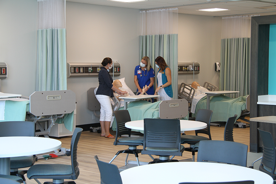 professor and student in classroom taking pulse rate of a maniken in a hospital bed