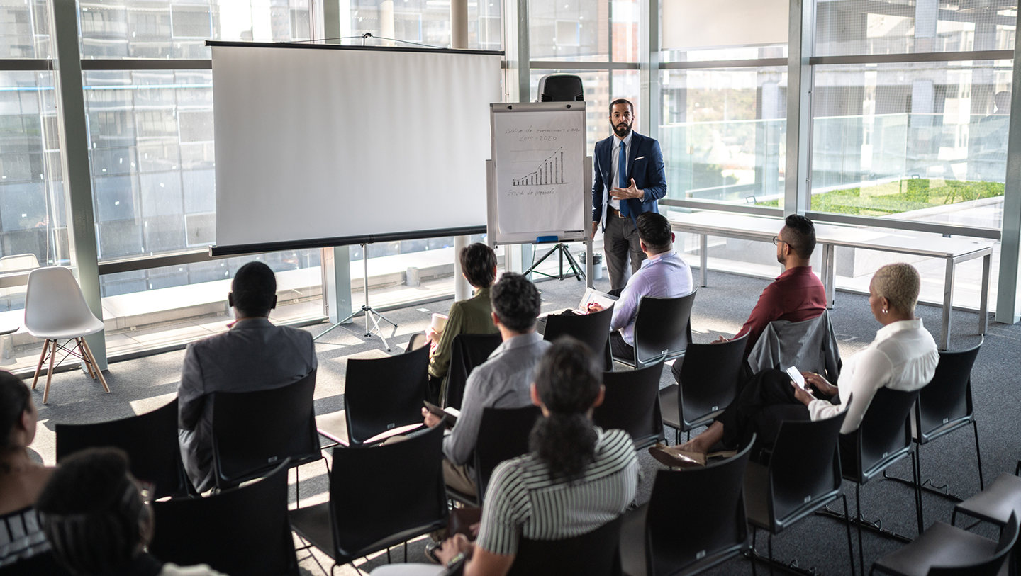 A man gives a presentation on a projection screen in front of a small audience