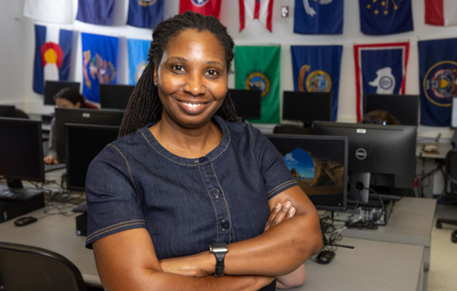 Tameka Johnson-Tillman standing in classroom with computers and a wall of flags in background