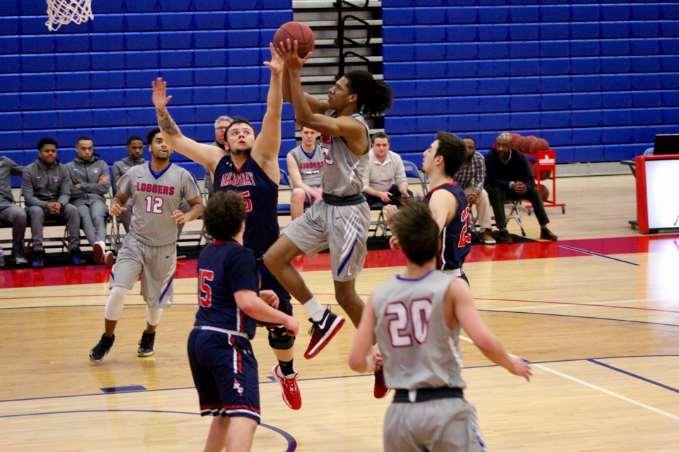 An LLCC men's basketball player makes a jump shot towards the hoop while being blocked by the opposing team. 