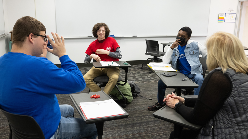 four student sitting in desks in a circle playing a game