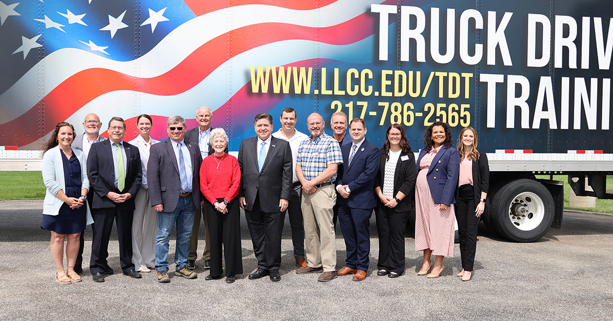 Governor, LLCC president and others standing in front of LLCC semi truck and trailer that features American flag and words Truck Driver Training