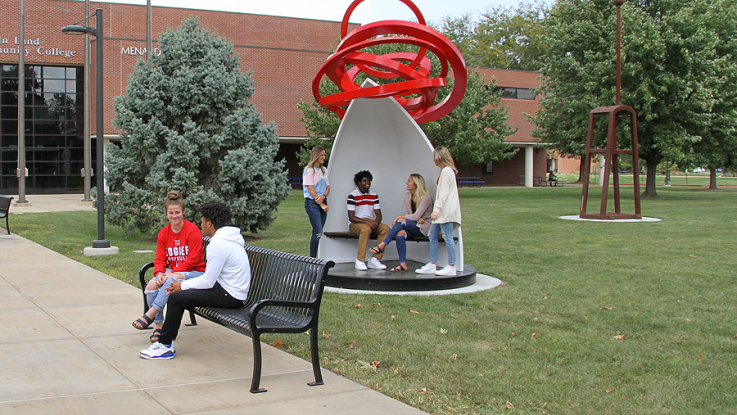 Students sitting on bench in sculpture and on bench on sidewalk