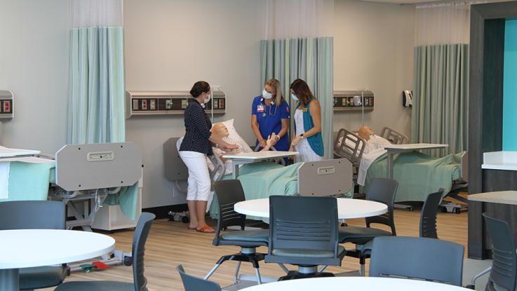 professor and student in classroom taking pulse rate of a maniken in a hospital bed