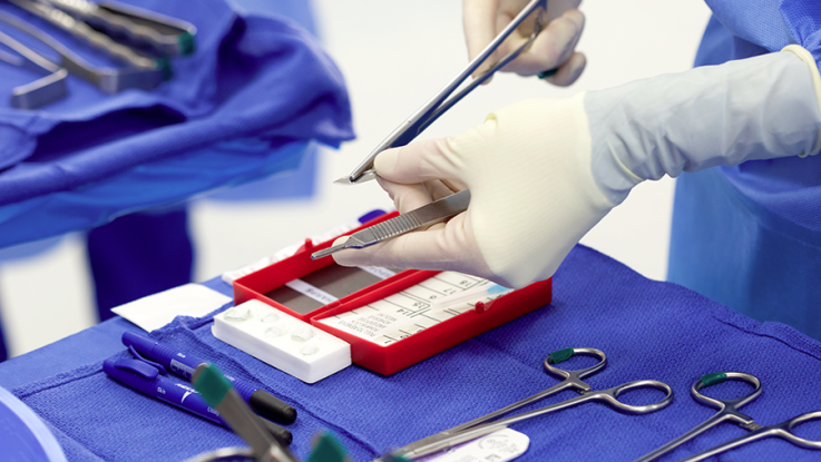 A close up of a hand in a white glove preparing surgical instruments.