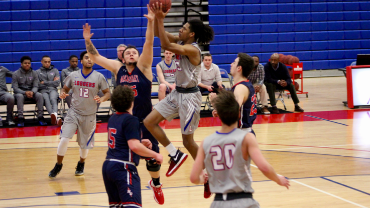 An LLCC men's basketball player makes a jump shot towards the hoop while being blocked by the opposing team. 