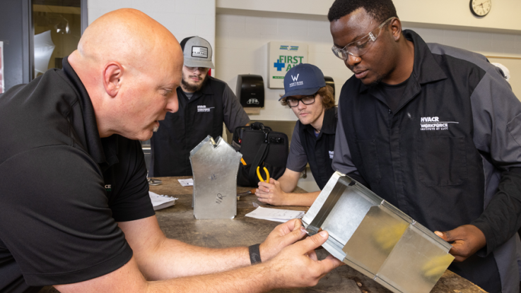 HVAC instructor with HVAC students looking at metal part