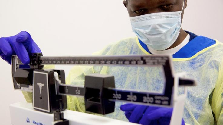 CNA student in scrubs, mask and gloves working a scale