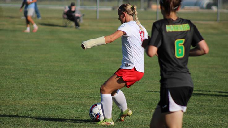 An LLCC women's soccer player kicks the ball while a player from the opposing teams runs toward her.
