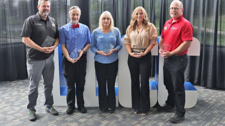 Five people stand for a photo holding awards.