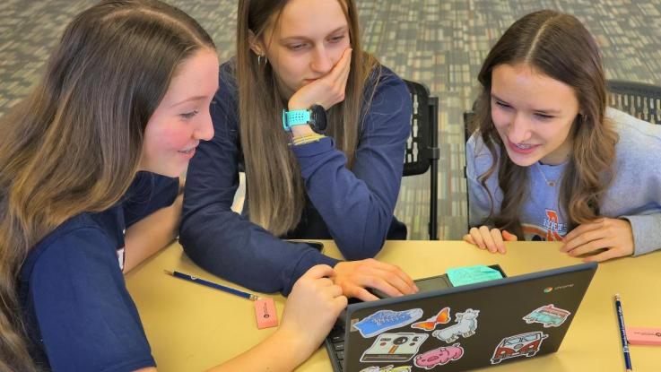 Three female students study over a laptop computer.