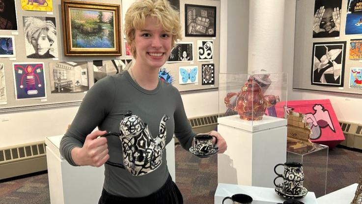 An art student holding a ceramic tea cup and kettle.