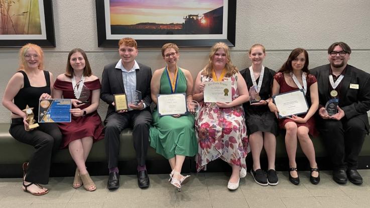 Eight people sitting in a row holding certificates and smiling.