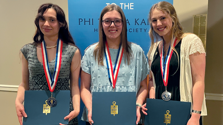 Three female students wearing medals smile for a photo.