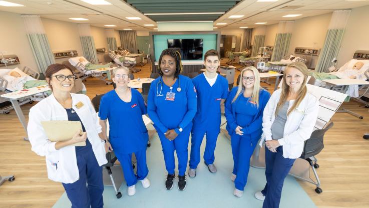 four nursing students in blue scrubs pose with their nursing instructors.