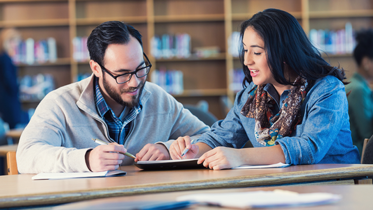 Two adults sit in a library and study school work.