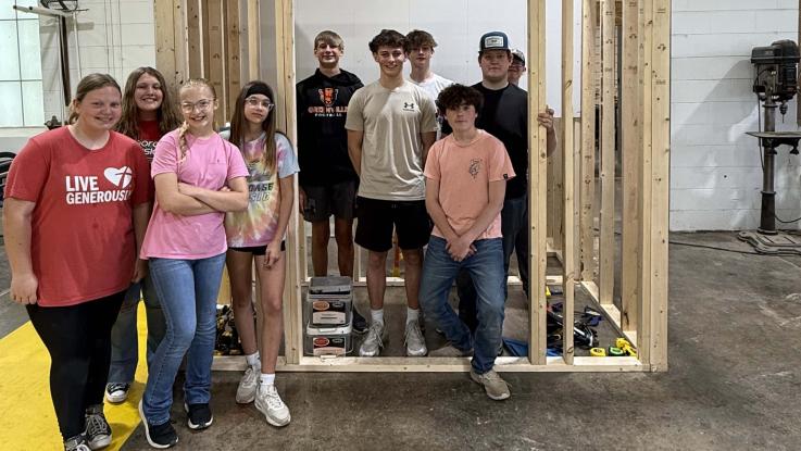 Group of eighth grade students standing in and around framed structure