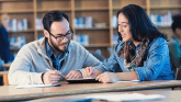 Two adults sit in a library and study school work.