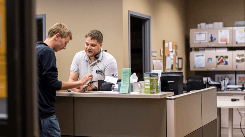 customer at a desk asking employee at a front desk for tech support on his tablet
