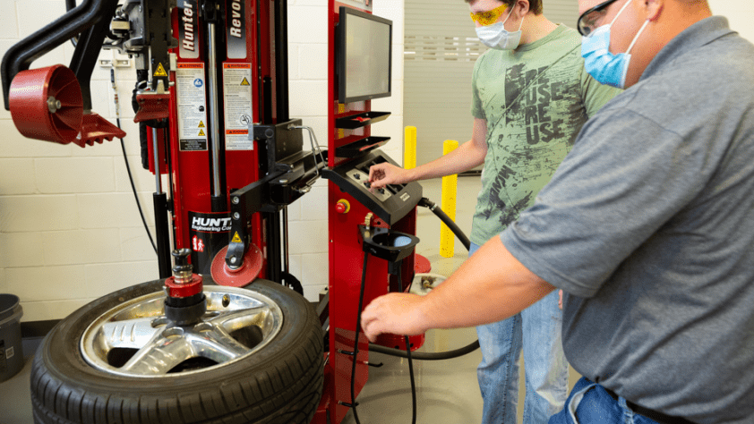 A student works inside a car while an instructor watches.