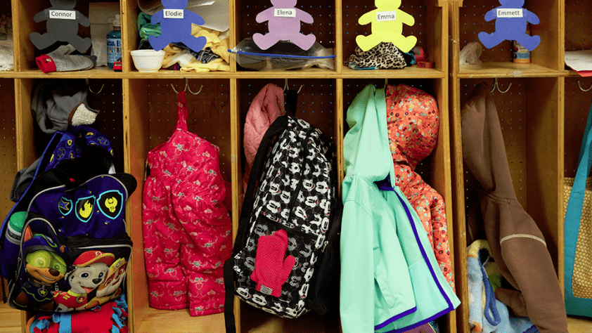 children's coats and backpacks under their names at a school or daycare