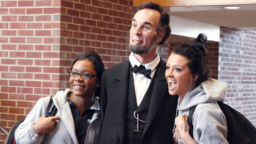 two female students standing with an Abraham Lincoln impersonator