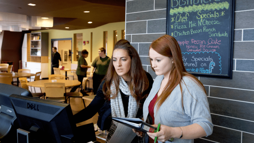 Sheridan Lane, director of operations, and a student review information on a computer at the front of Bistro Verde Cafe in Workforce Careers Center.