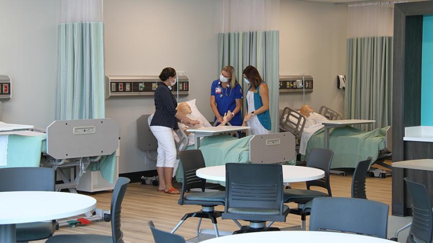 professor and student in classroom taking pulse rate of a maniken in a hospital bed