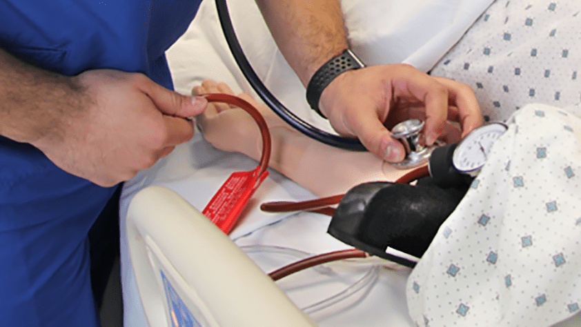 male student checking pulse rate on arm with stethoscope