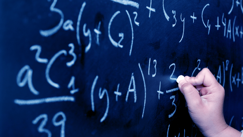 instructor's hand with chalk, writing math equations on a chalkboard