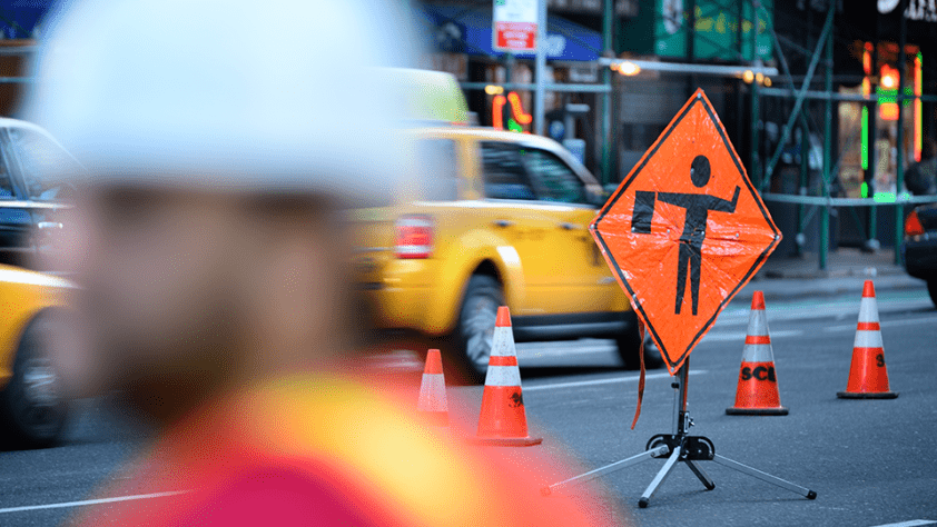 blurry construction worker on a busy street with construction signs and cones