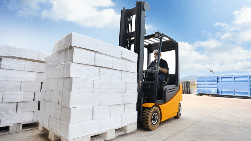 A person moves pallets with a forklift outside.