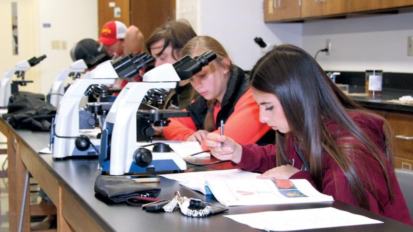 Students with microscopes in a biology lab classroom.