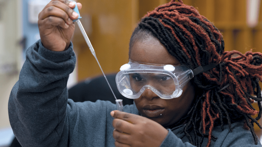 student wearing eye protection with test tube and dropper in a science lab