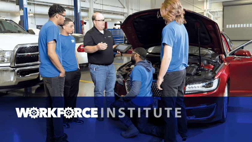 Instructor talking to four students near car with hood up in auto tech lab. Workforce Institute.