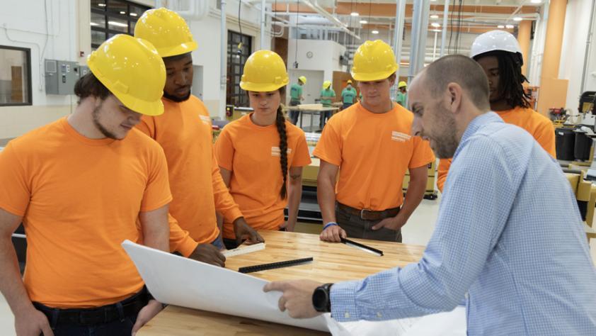 student with hard hats in the construction lab with instructor looking at blueprints