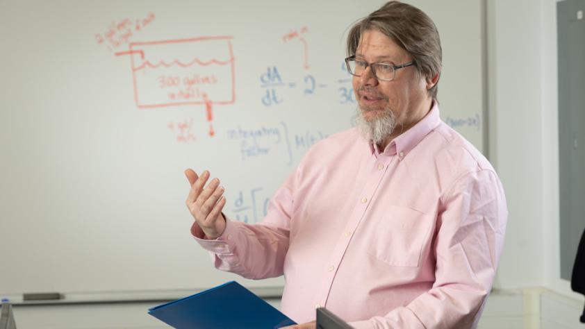 professor in front of white board that has math equations written on it