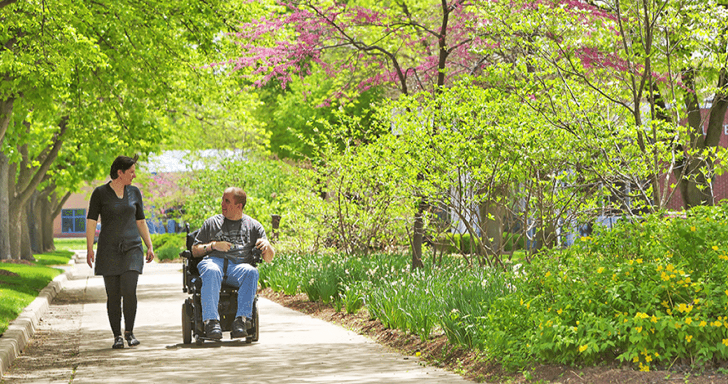 student walking next to student in wheelchair on campus