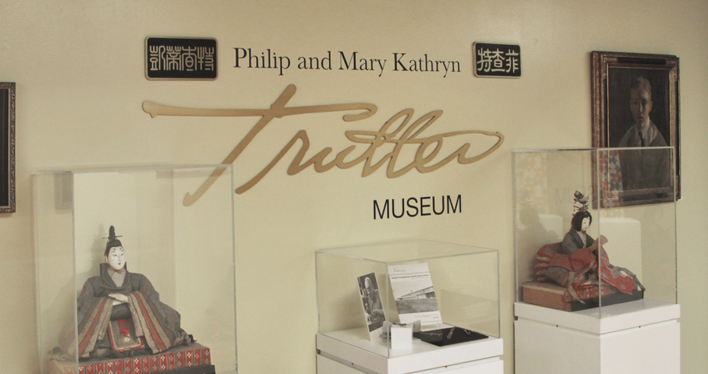 Three pieces of art in display cases in front of a wall that says Philip and Mary Kathryn Trutter Museum.