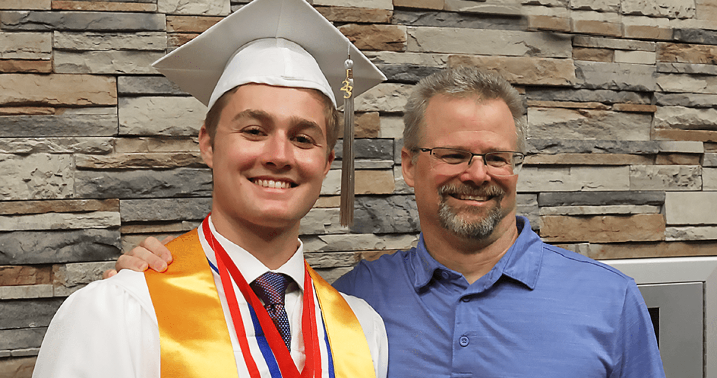 LLCC graduate in regalia standing next to his dad