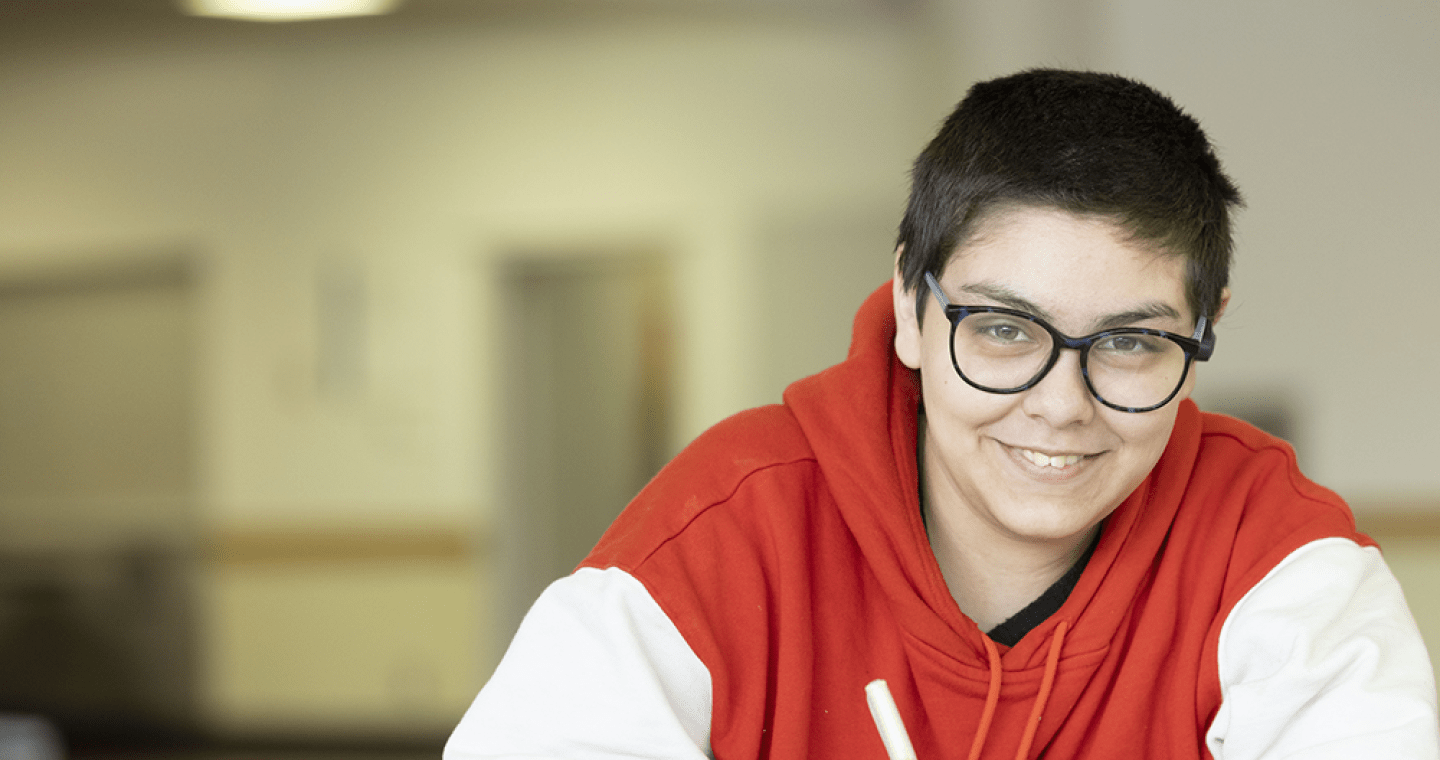 Student in a red and white jacket smiling at the camera.
