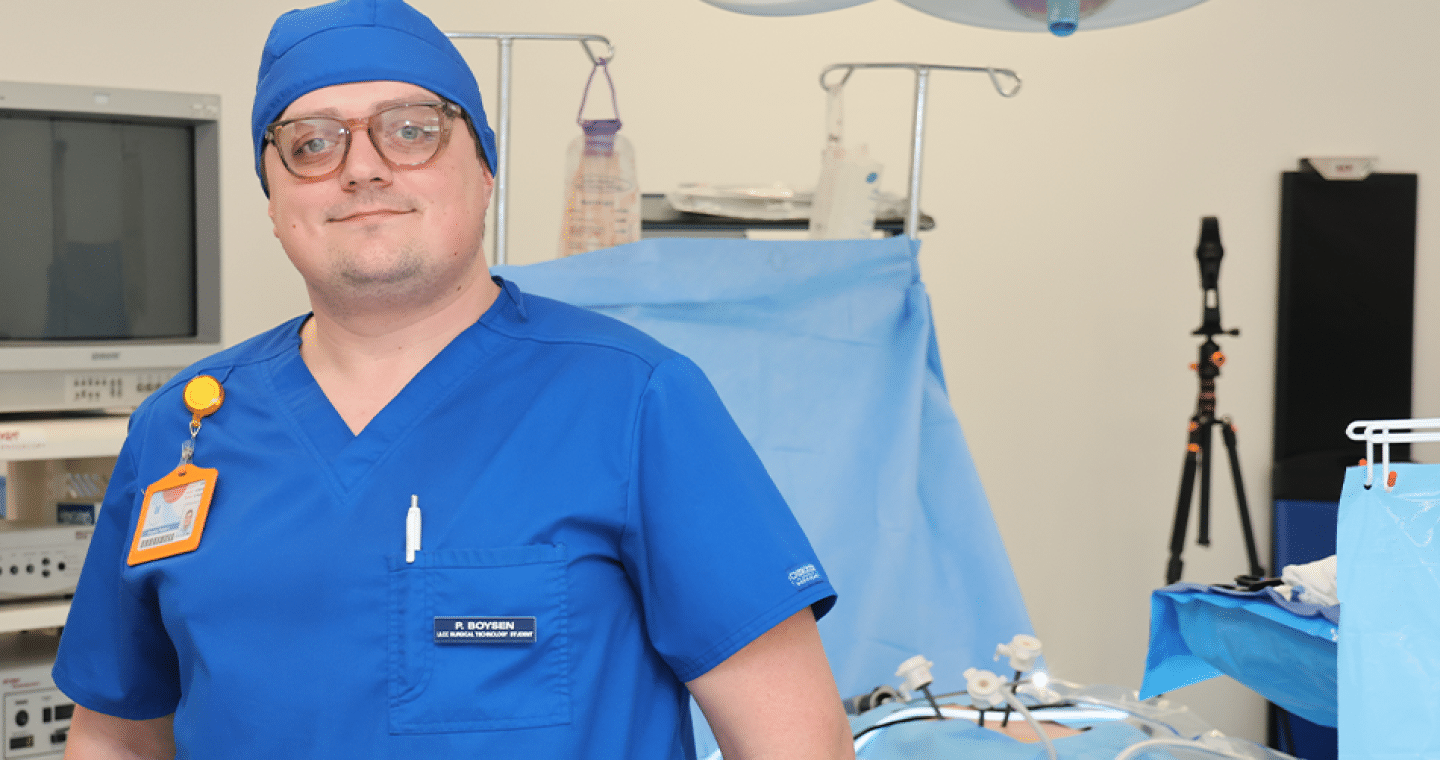 male student in blue scrubs standing in an operating room