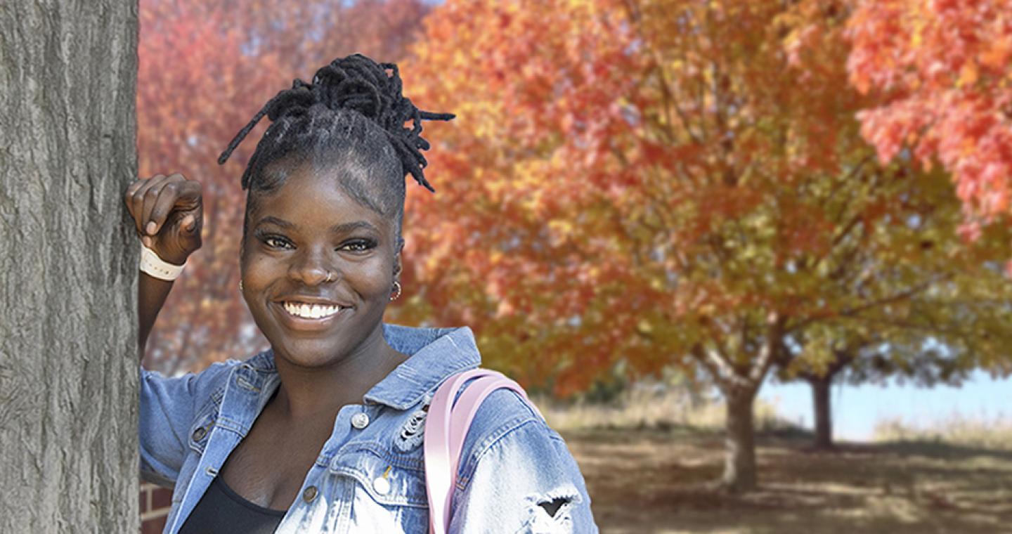 Student standing outside with trees with fall coloring in background
