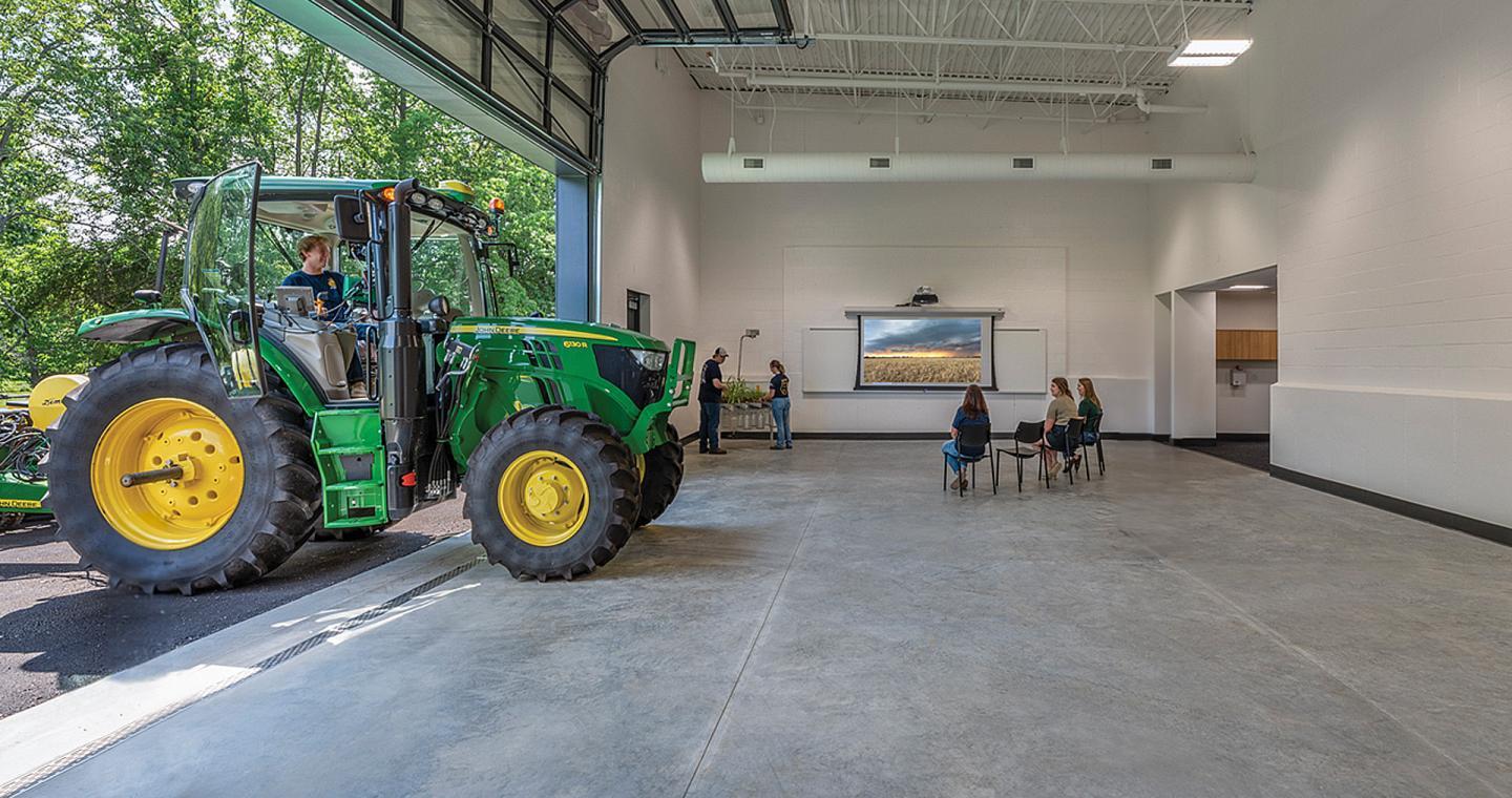 student driving tractor into garage bay