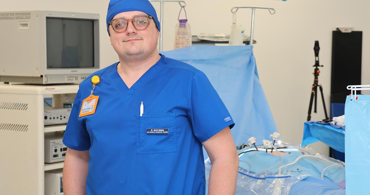 Male student in blue scrubs standing in an operating room