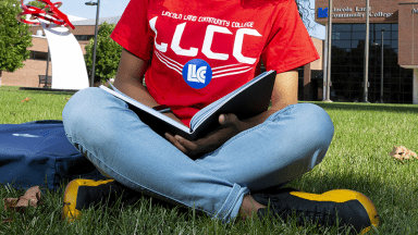 Student in LLCC T-shirt sitting on grass outside campus building