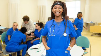 a smiling student standing in a classroom with other students behind her